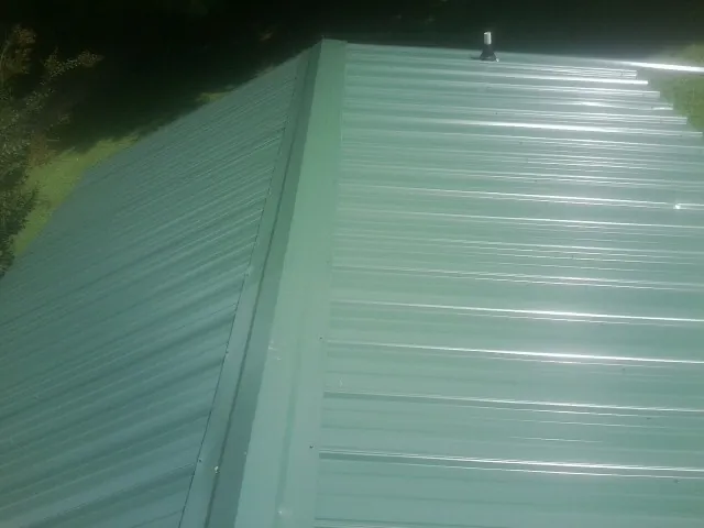 New green metal panels meeting at the ridge of a roof — Flat Roof Repair work by our crew in Gas City