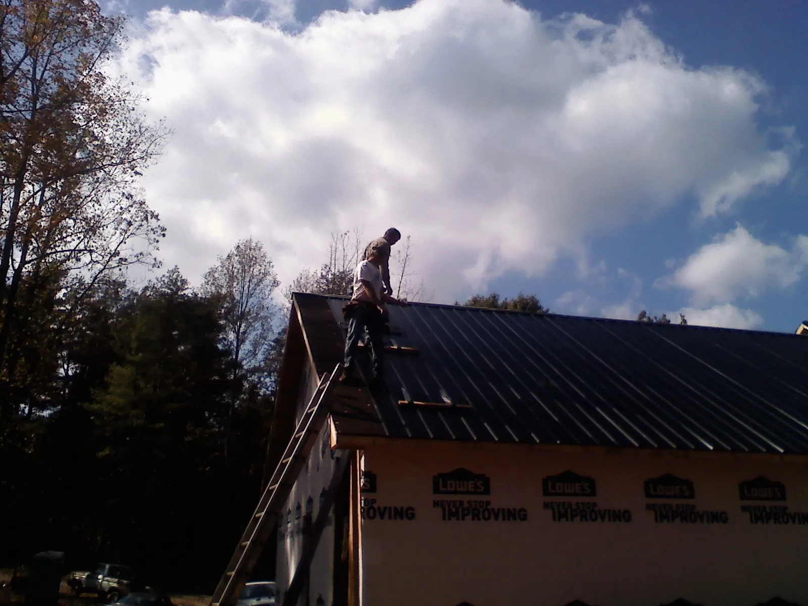 Roofer fastening dark metal panels high against a cloudy sky, from a Roof Inspection job in Gas City