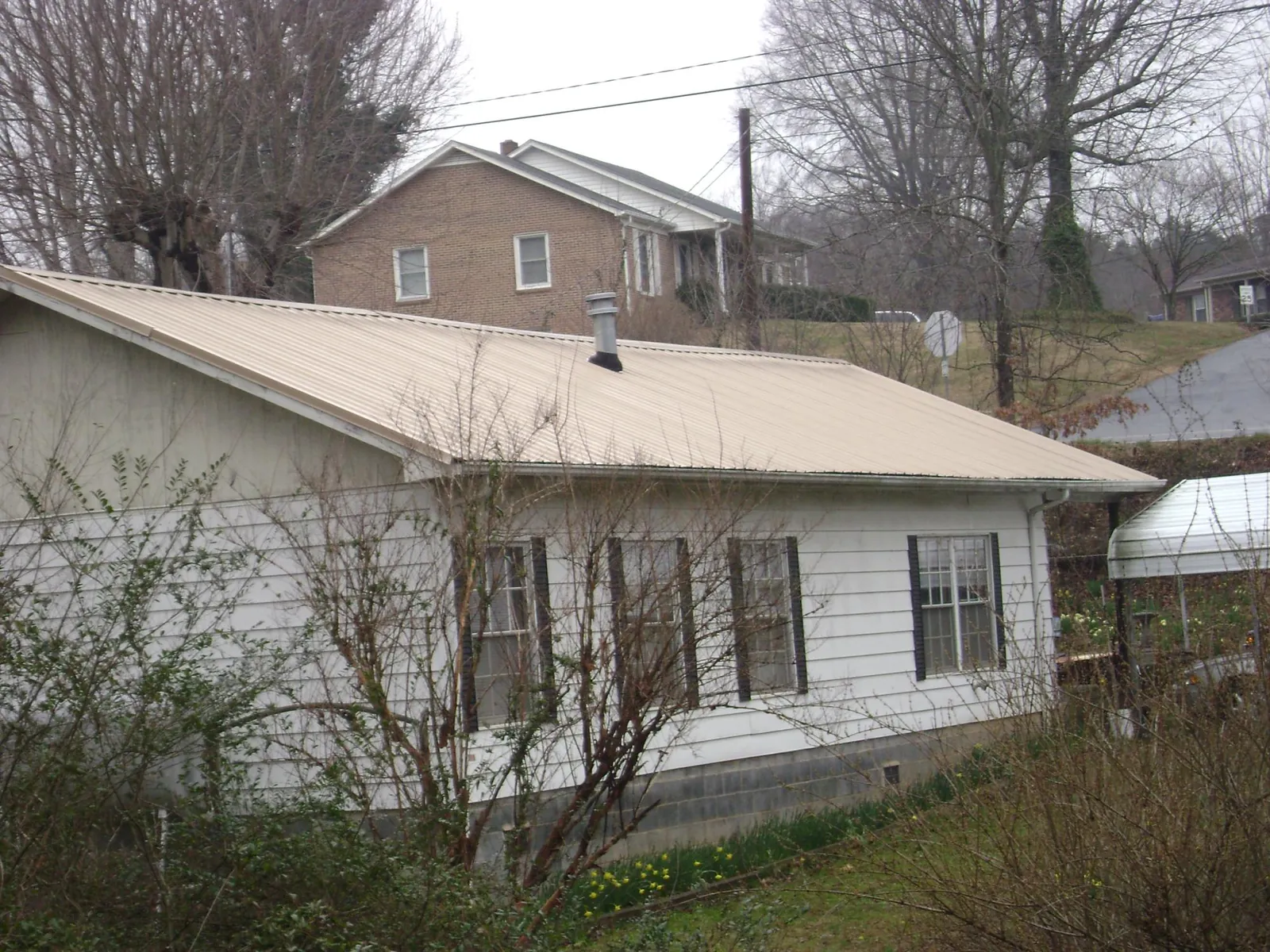 Tan metal roof on a white sided house set into a hillside — Commercial Roofing by Roofing Brothers in Gas City